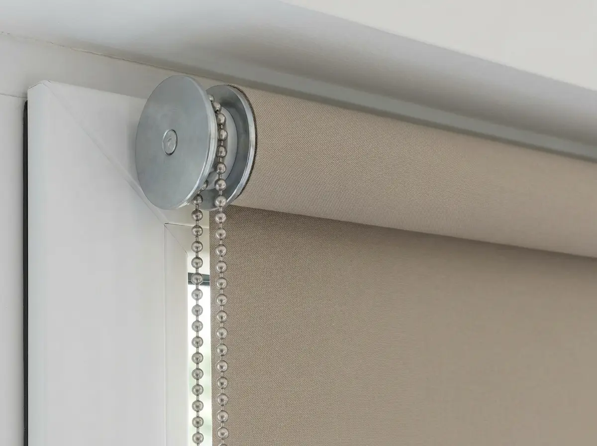 Close-up of a roller blind chain-control mechanism and flat taupe fabric roll mounted on a window frame in Wellington